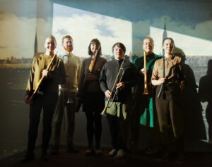 Sechs Musiker und Musikeronnen stehen nebeneinander mit ihren Instrumenten in der Hand vor einer Tapete mit einer Bremer Stadtansicht.