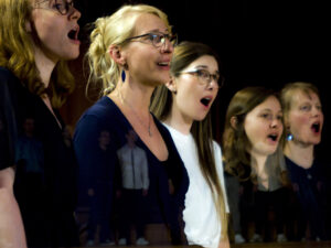 Großaufnahme von Sängerinnen mit weit geöffneten Mund in einer diagonalen Reihe.