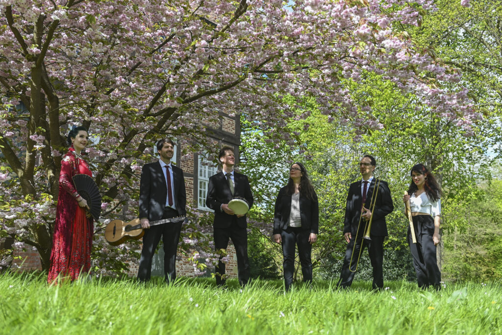 Musiker und Musikerinnen von Concierto Iberico stehen mit der Tänzerin unter einem blühenden Kirschbaum in einem Garten.