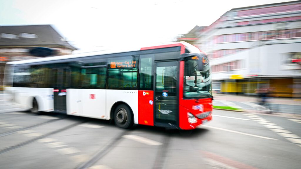 Ein rot-weißer Bus der Bremer Straßenbahn AG fährt von links nach rechts über eine Straßenkreuzung. Der Bus und der Hintergrund sind verschwommen.